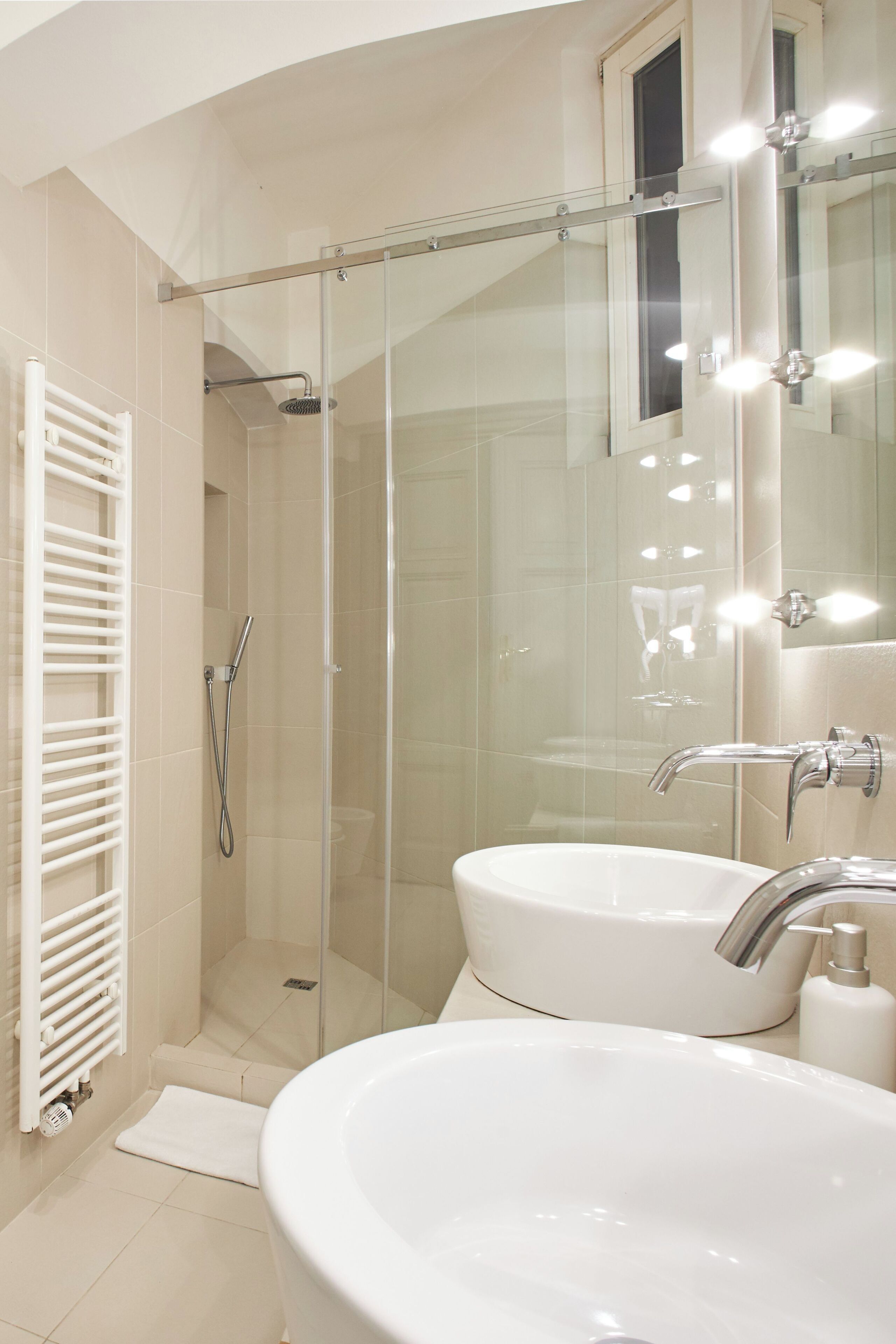 A modern bathroom with a glass-enclosed shower, two sinks, and a white radiator.