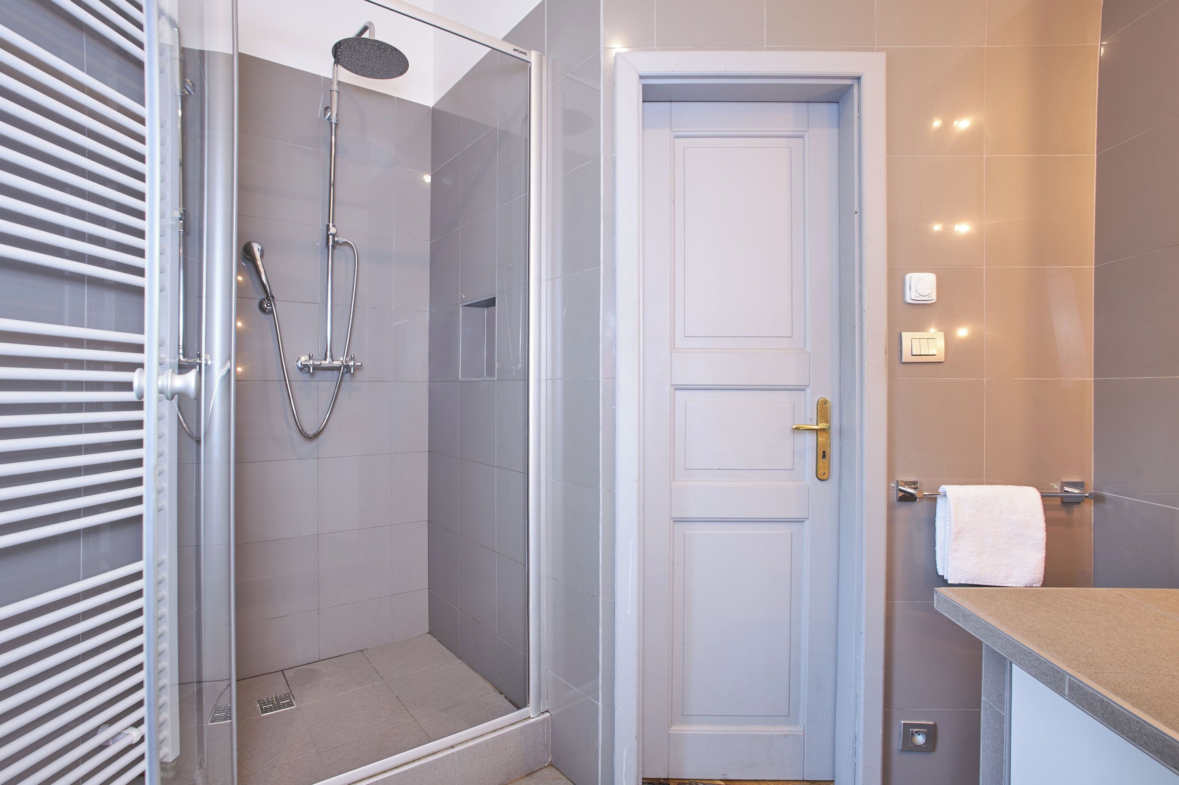 A modern bathroom with a glass-enclosed shower, a white door, and a countertop with a towel.