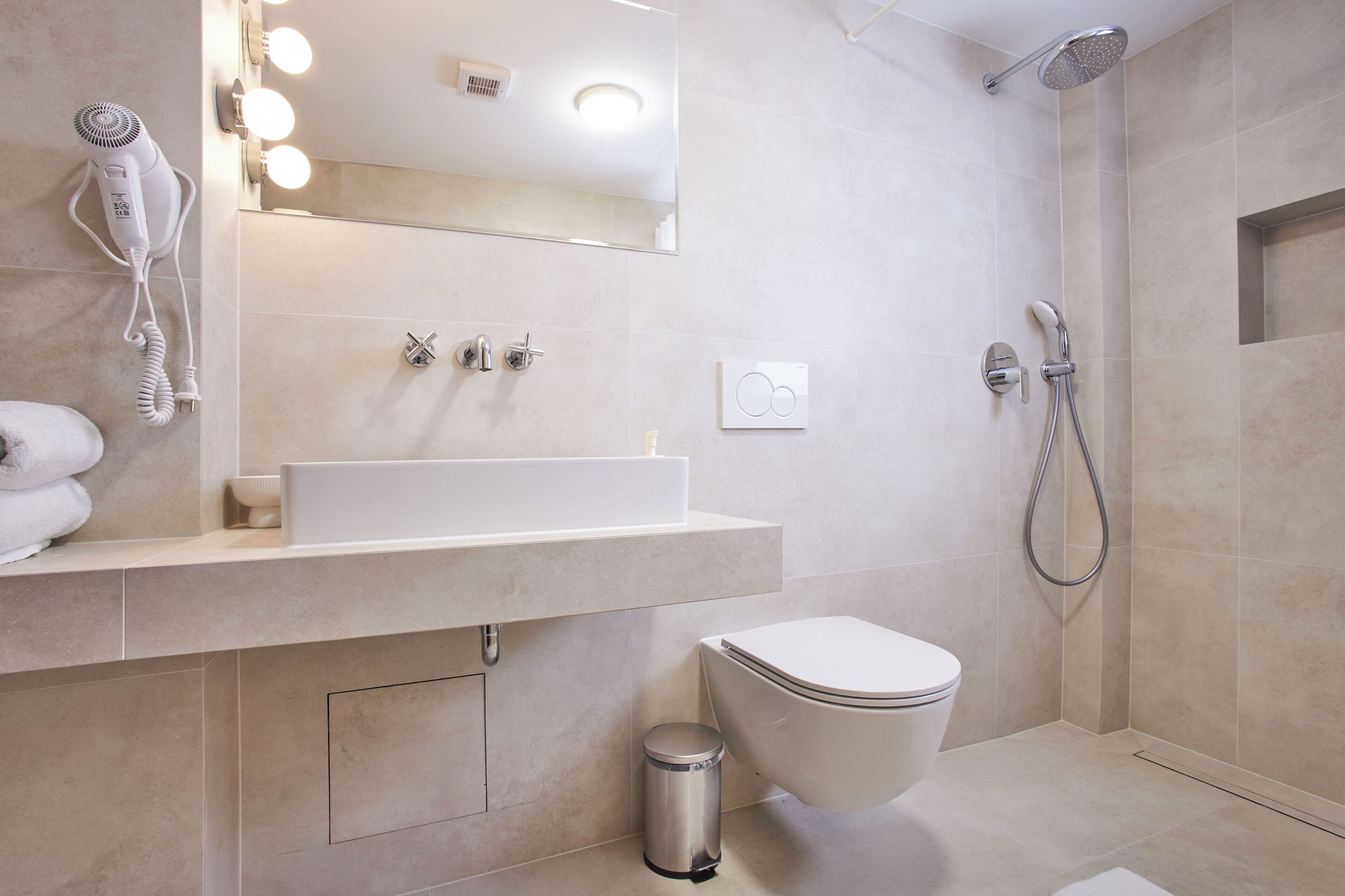 A modern bathroom with a white sink, a toilet, a shower, and a hairdryer mounted on the wall.