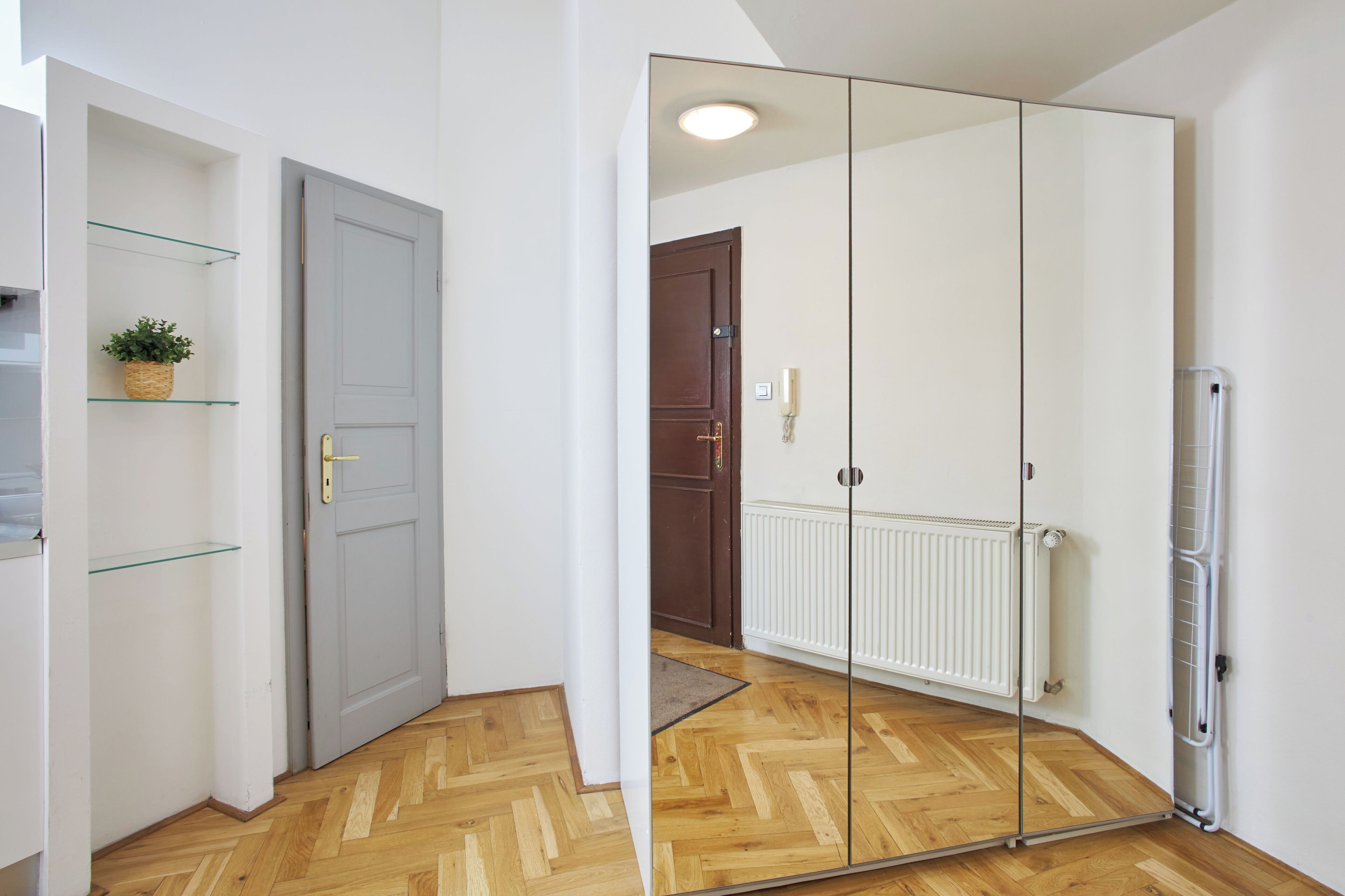 Una habitación con armario espejado, suelo de madera, radiador y puerta con picaporte.