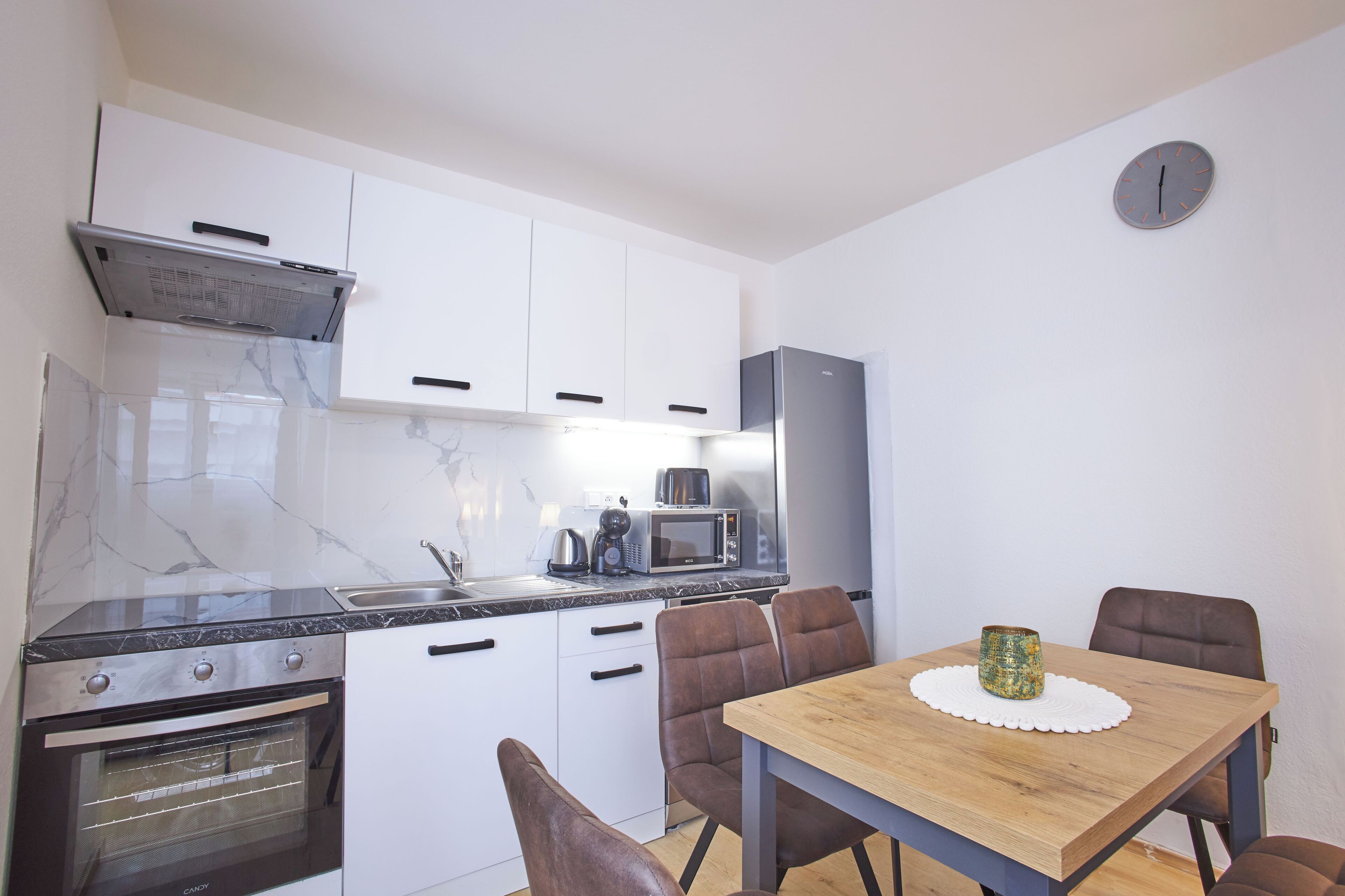 A compact kitchen with white cabinets, a microwave, a stove, and a dining table with four chairs.