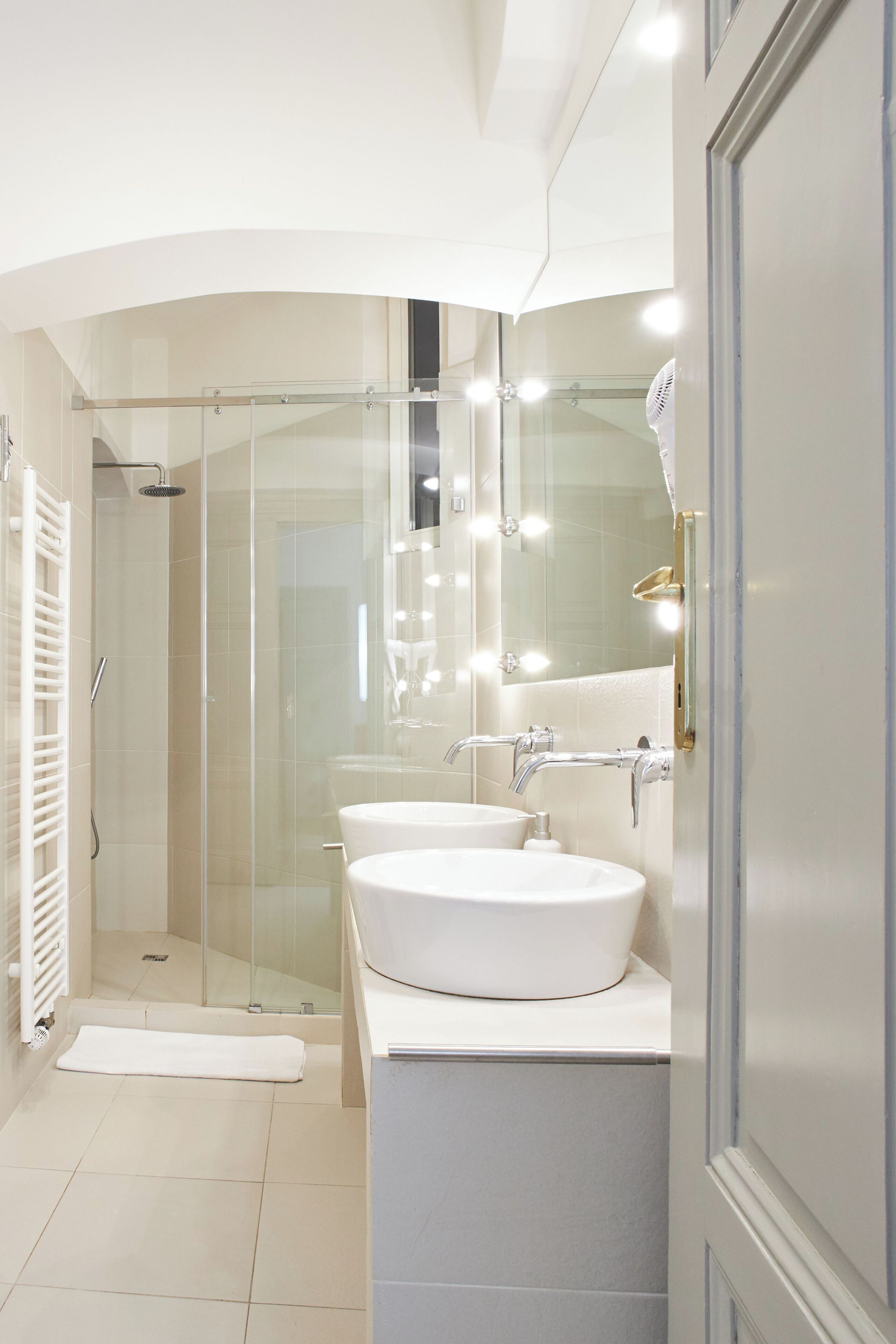 Une salle de bain moderne dotée d’une douche à parois de verre, de deux lavabos et d’un meuble-lavabo avec un miroir.