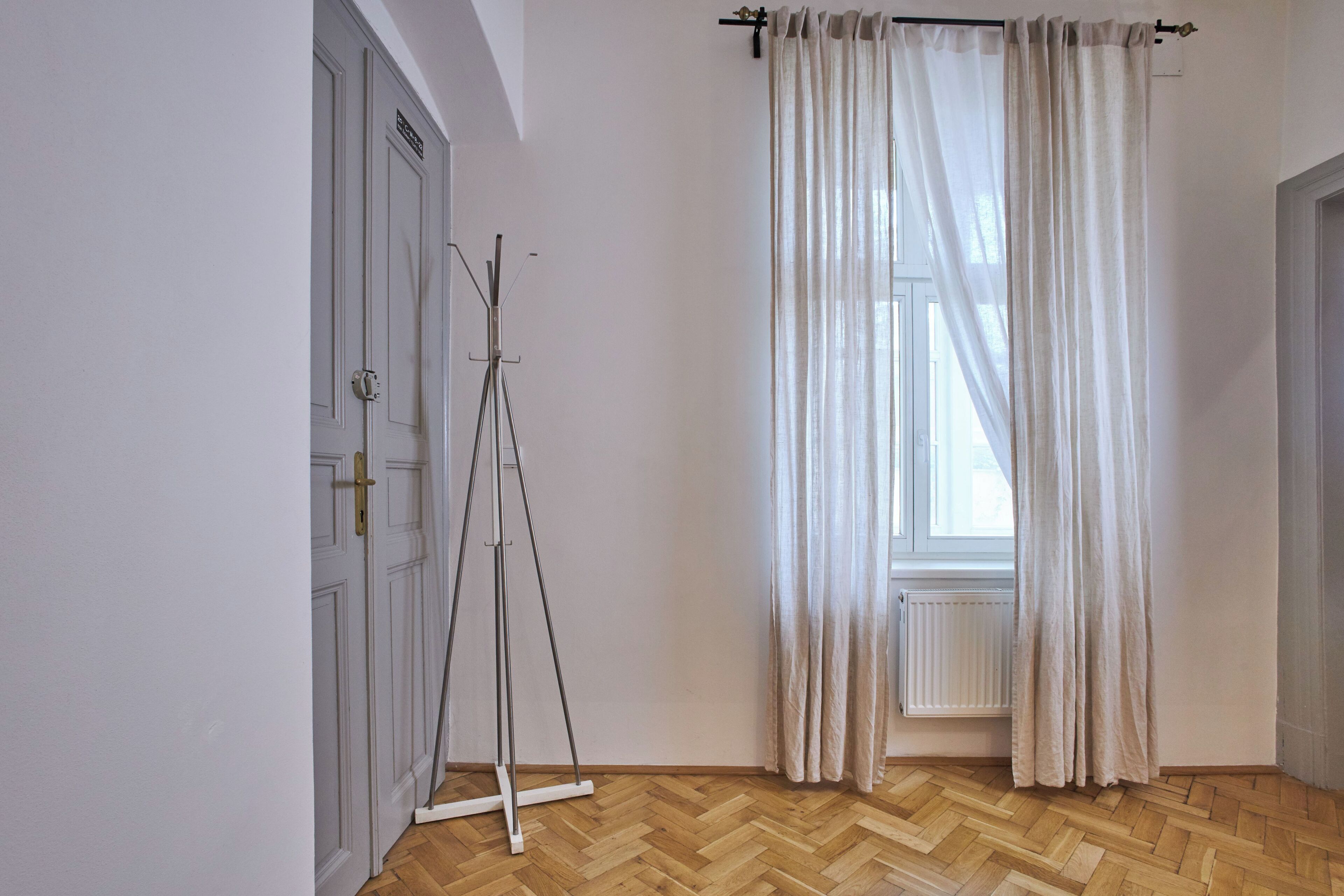 A room with a wooden herringbone floor, a white door, and a window with sheer curtains.