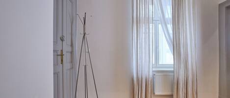 A room with a wooden herringbone floor, a white door, and a window with sheer curtains.