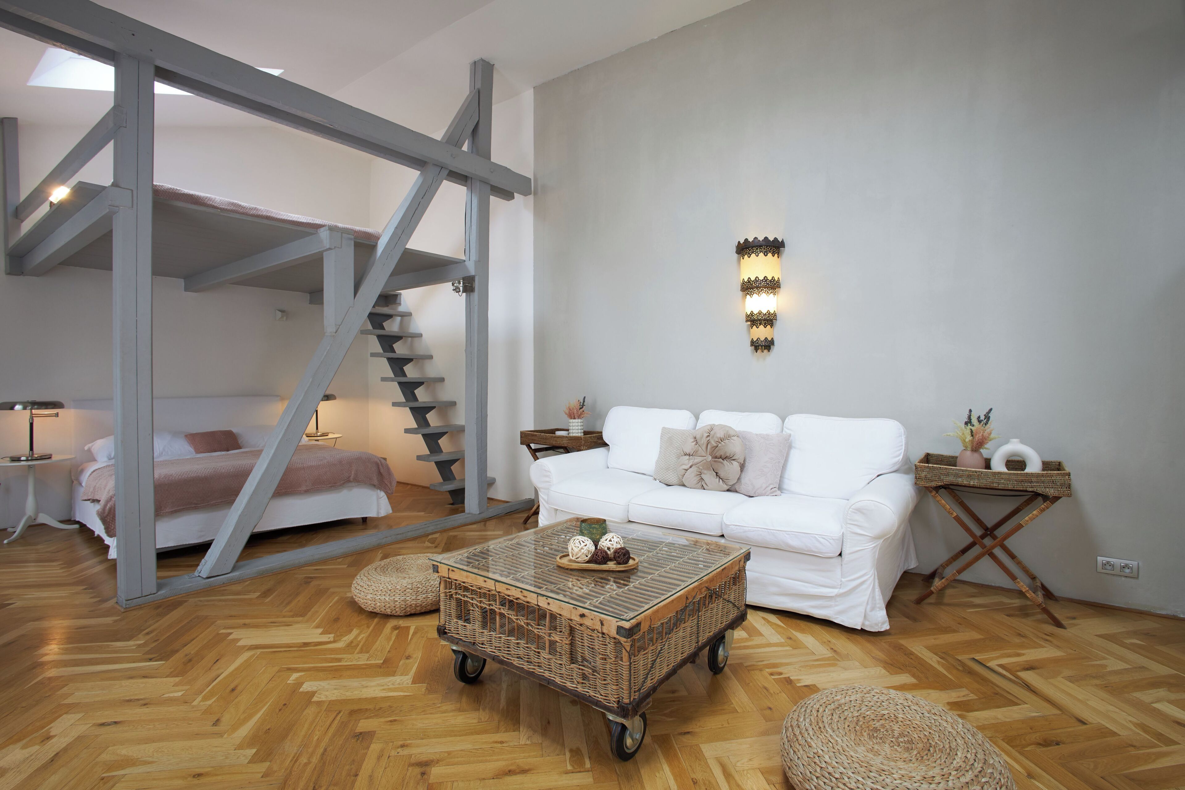 Una sala de estar moderna con un sofá blanco, una mesa de centro de madera, una cesta de mimbre y una escalera.