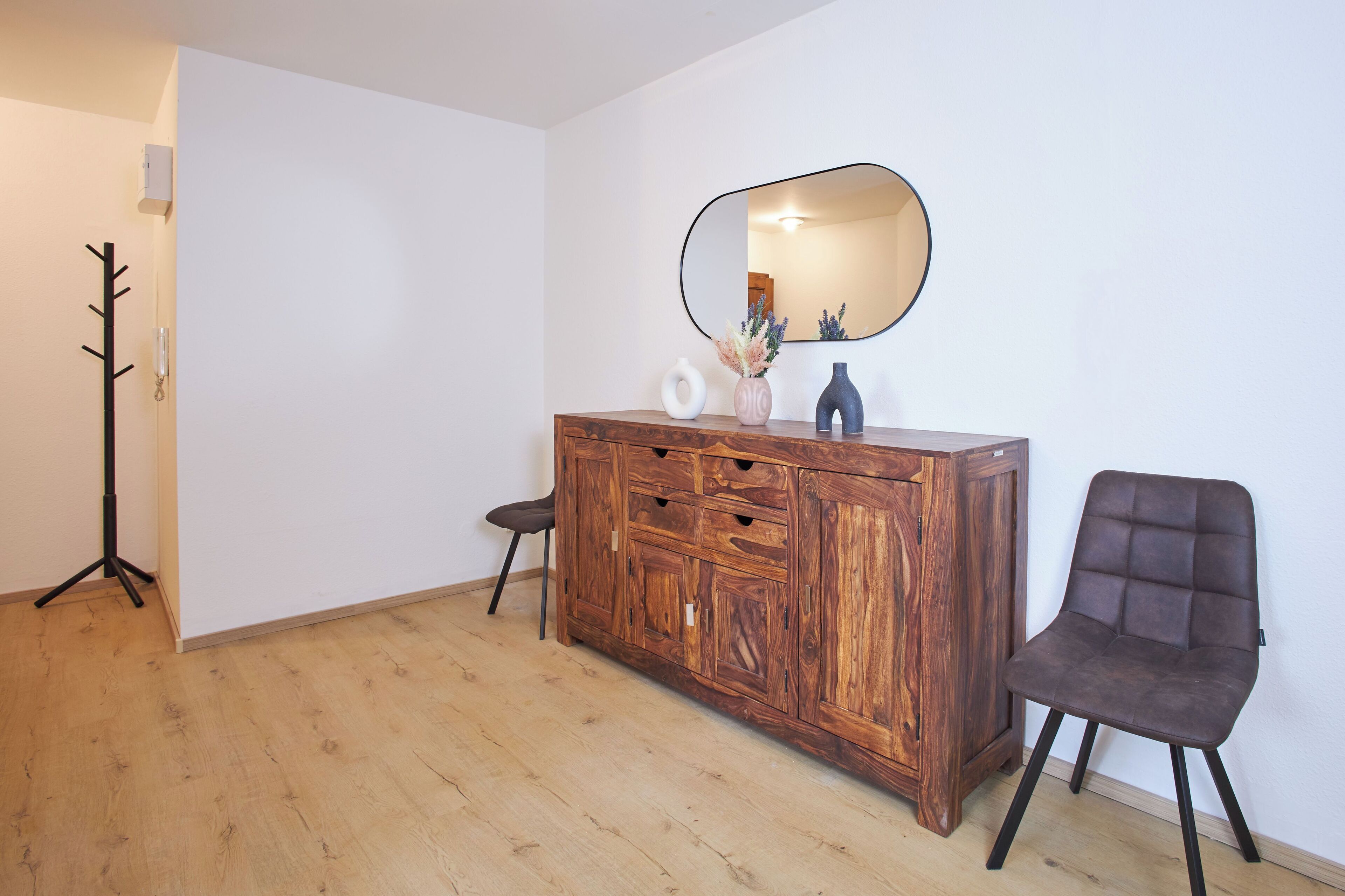 Une pièce comprenant un meuble en bois, une chaise, un porte-manteau et un miroir au mur.