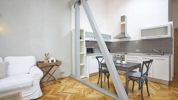 A compact living space with a kitchenette, a dining area with a table and chairs, and a white sofa.