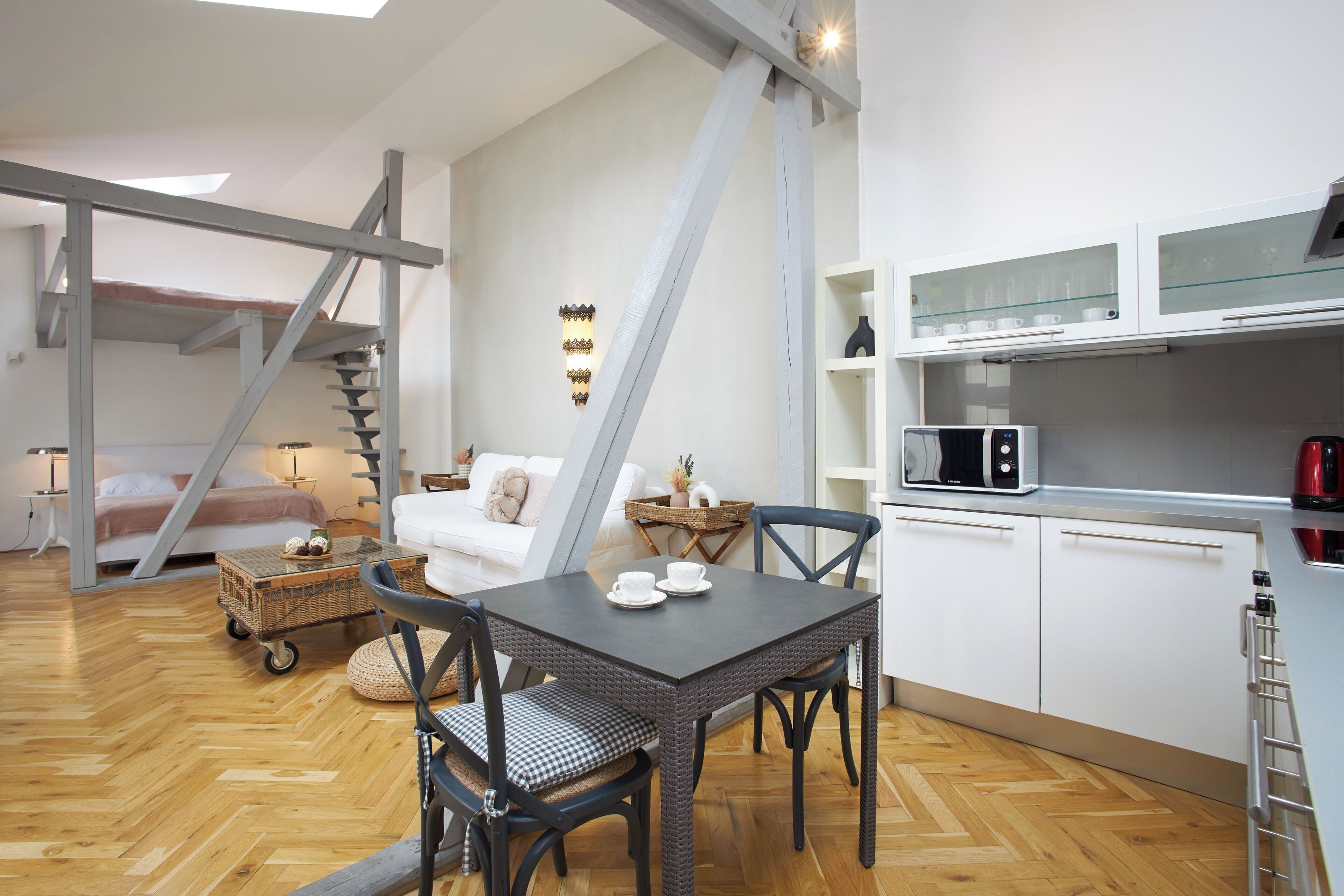 A compact living space with a loft bedroom, a dining area with a table and chairs, a kitchenette with a microwave, and a staircase.
