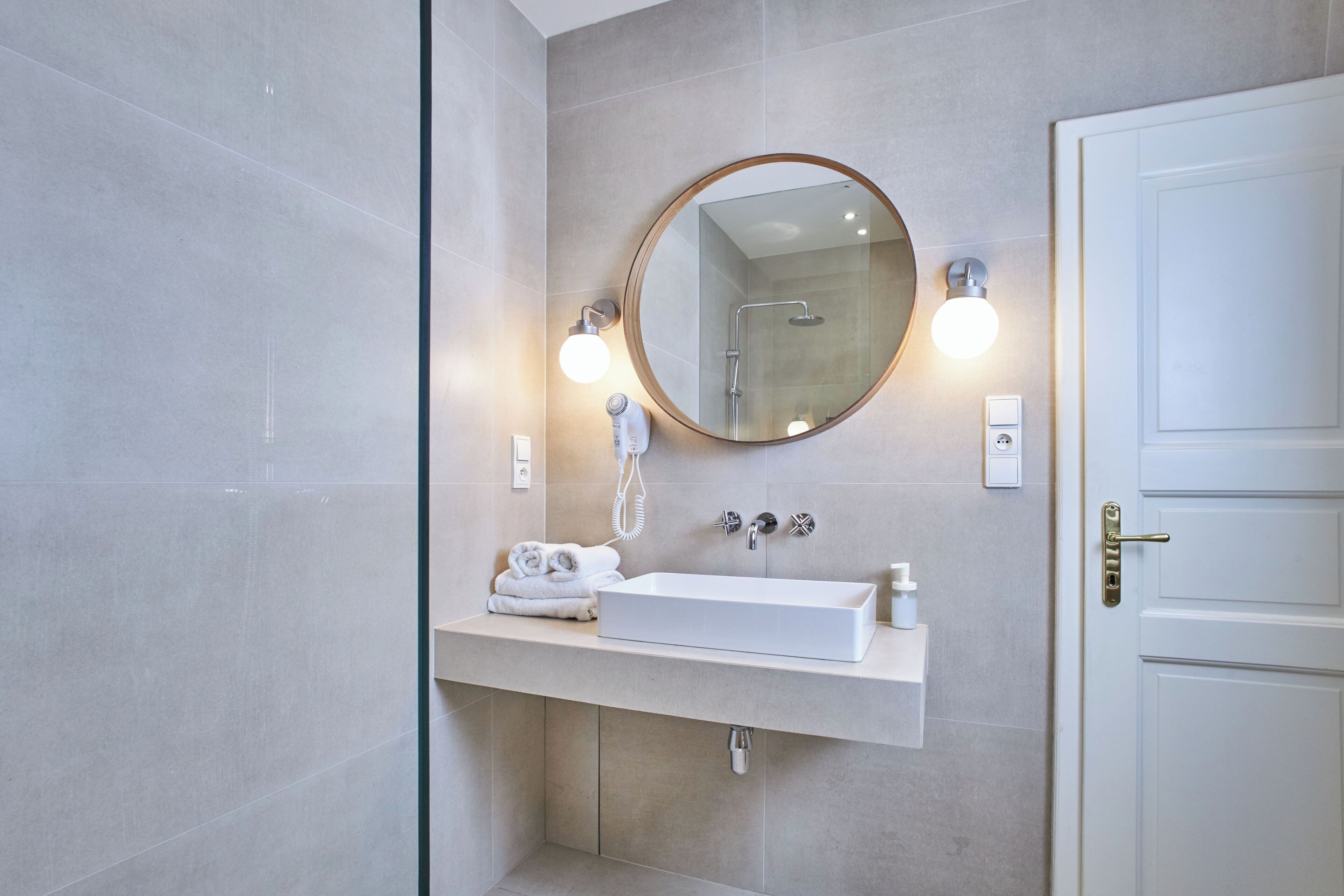 A modern bathroom with a rectangular sink, a round mirror, and two wall-mounted lights.