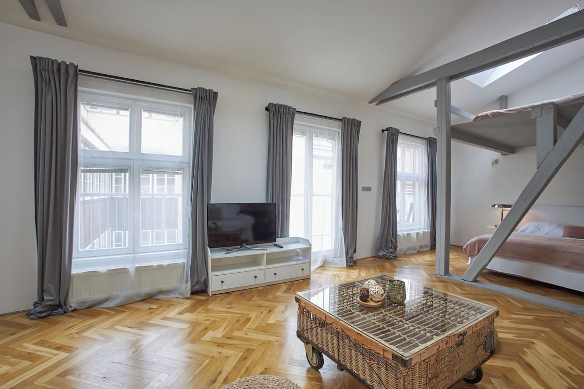 A spacious room with a large window, a television, a wooden floor, a wicker coffee table, and a bunk bed.