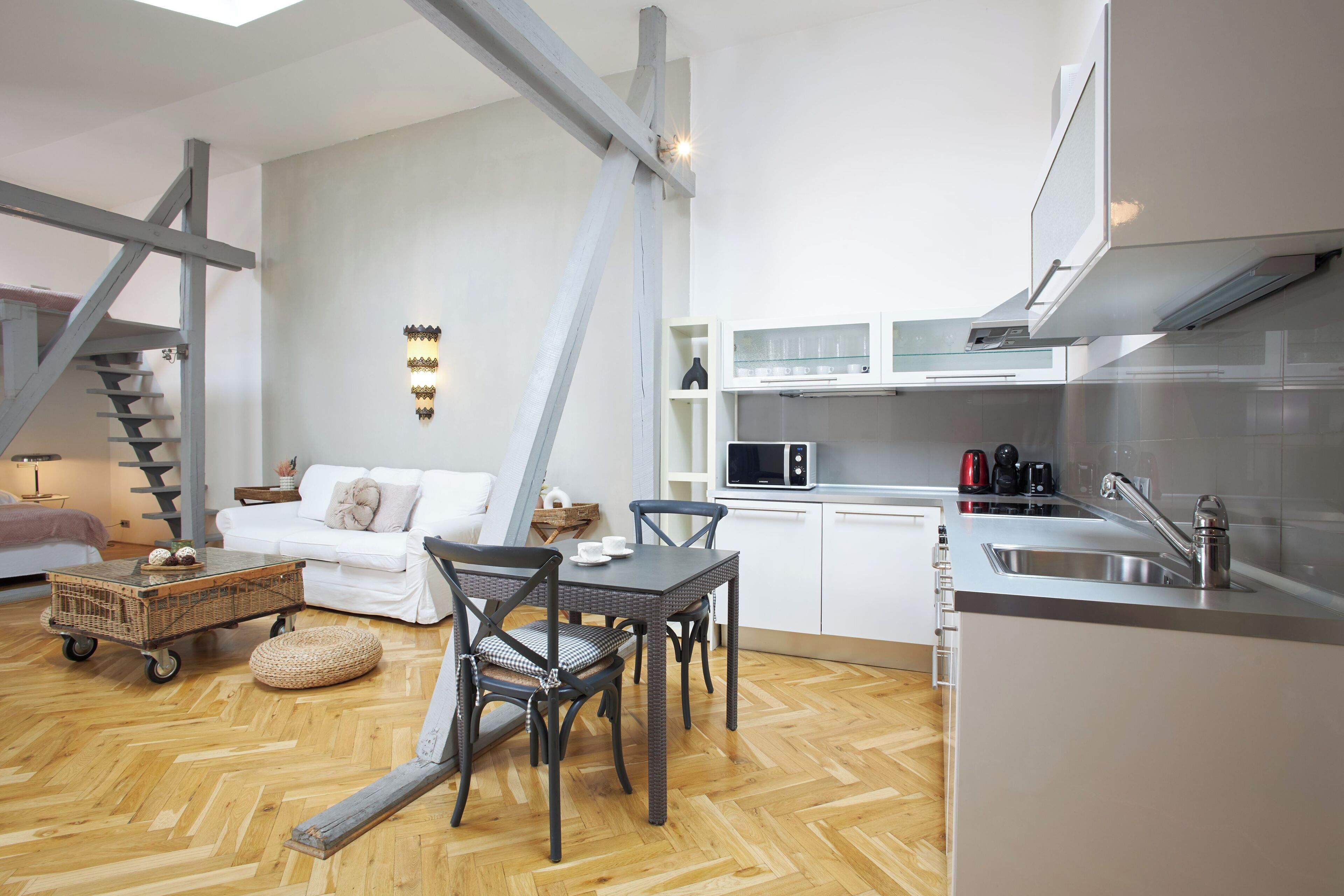 Een compacte leefruimte met een kitchenette, een eethoek met een tafel en stoelen, een bank en een trap.