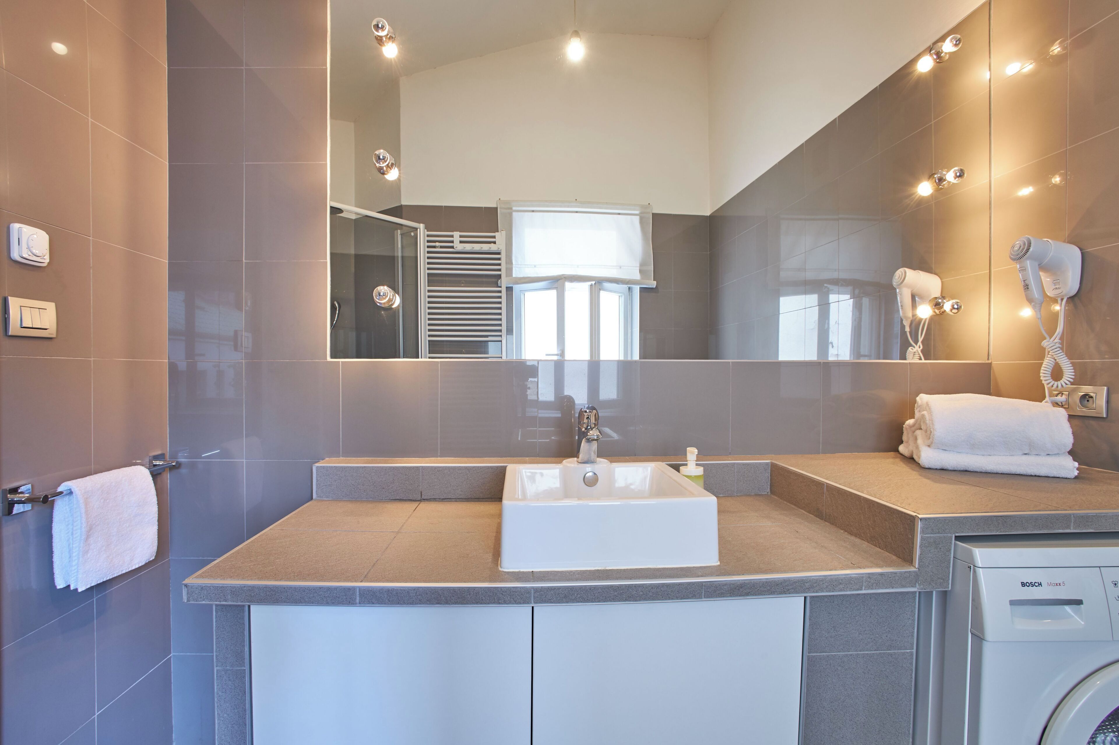 A modern bathroom with a sink, mirror, towel rack, and a Bosch washing machine.