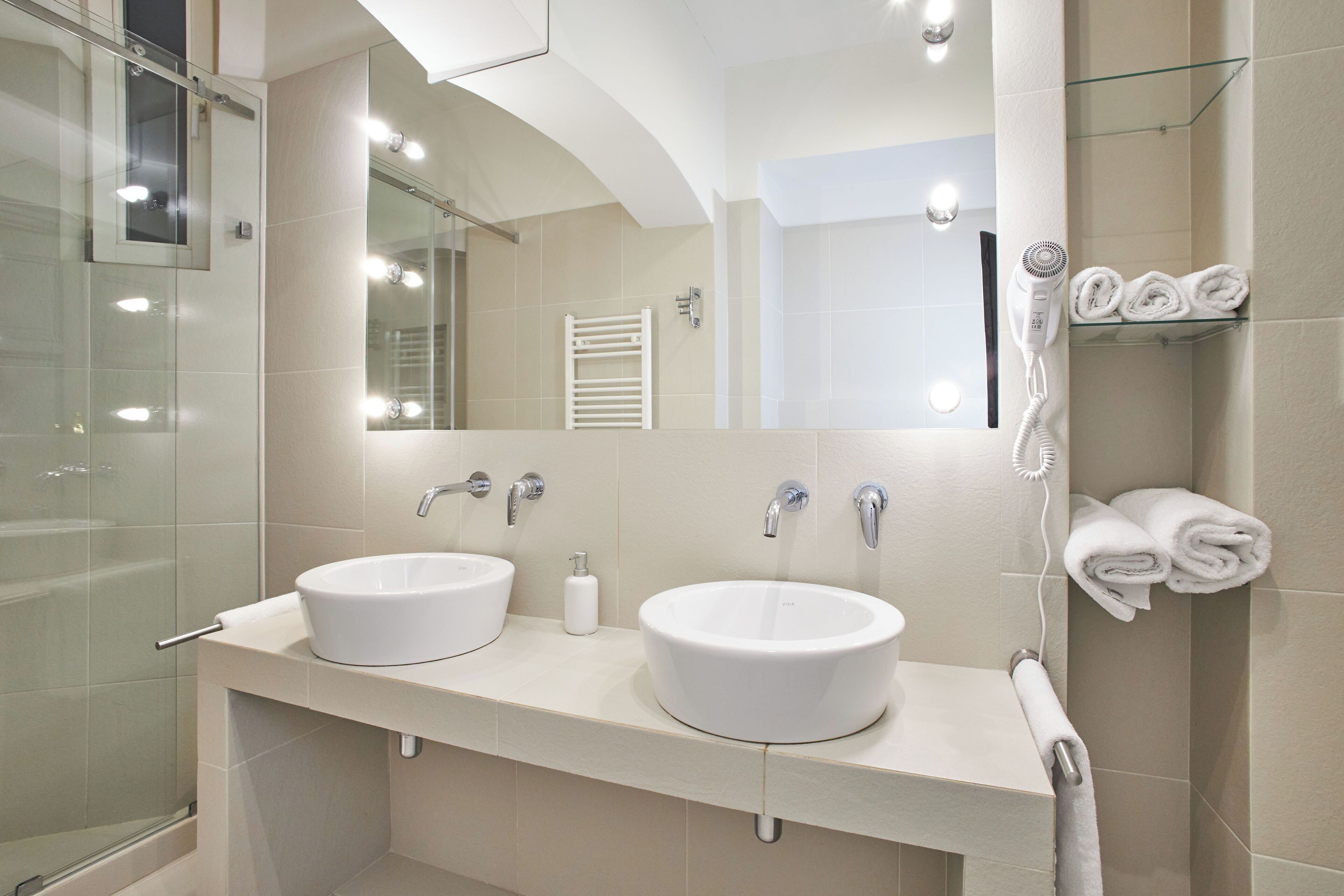 A modern bathroom with two sinks, a large mirror, and a glass shower enclosure.