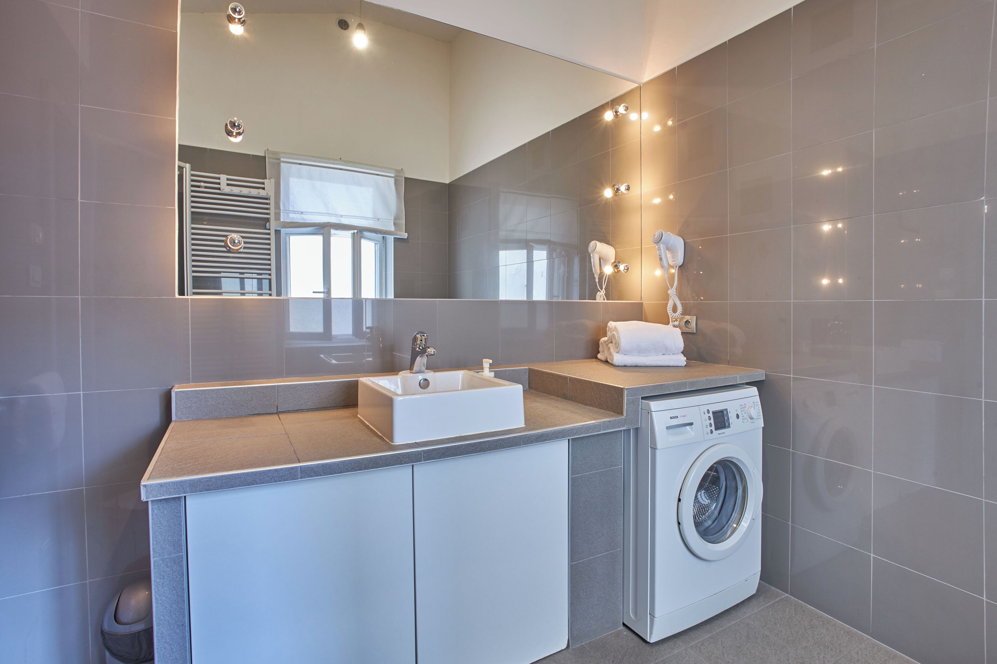 Een moderne badkamer met een grote spiegel, een wastafel, een wasmachine en een handdoekhouder.