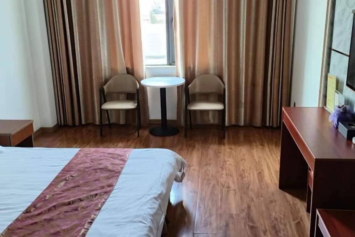 A hotel room with a bed, a small round table, two chairs, a wooden floor, and a TV on the wall.