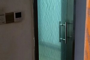 Una habitación con una puerta de cristal texturizado, un termostato en la pared y un objeto naranja parcialmente visible.