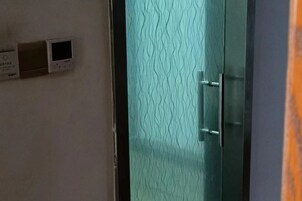 Una habitación con una puerta de cristal texturizado, un termostato en la pared y un objeto naranja parcialmente visible.