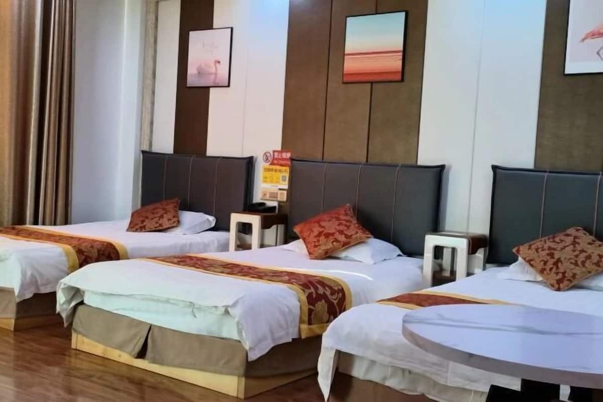 A hotel room with three beds, a small table, and a wall-mounted clock.
