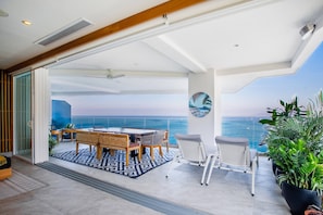 A spacious balcony with a view of the ocean, a dining area with a table and chairs, and potted plants.