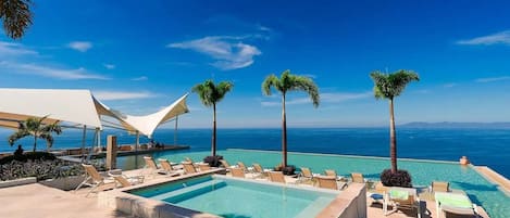 A resort pool area with sun loungers, a large pool, and palm trees.