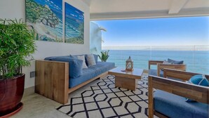 Ein modernes Wohnzimmer mit einer Couch, einem Couchtisch und Sesseln, einer großen Topfpflanze und Meerblick durch große Fenster.