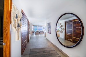 A hallway with wooden doors, a round mirror, and a view to a living area.