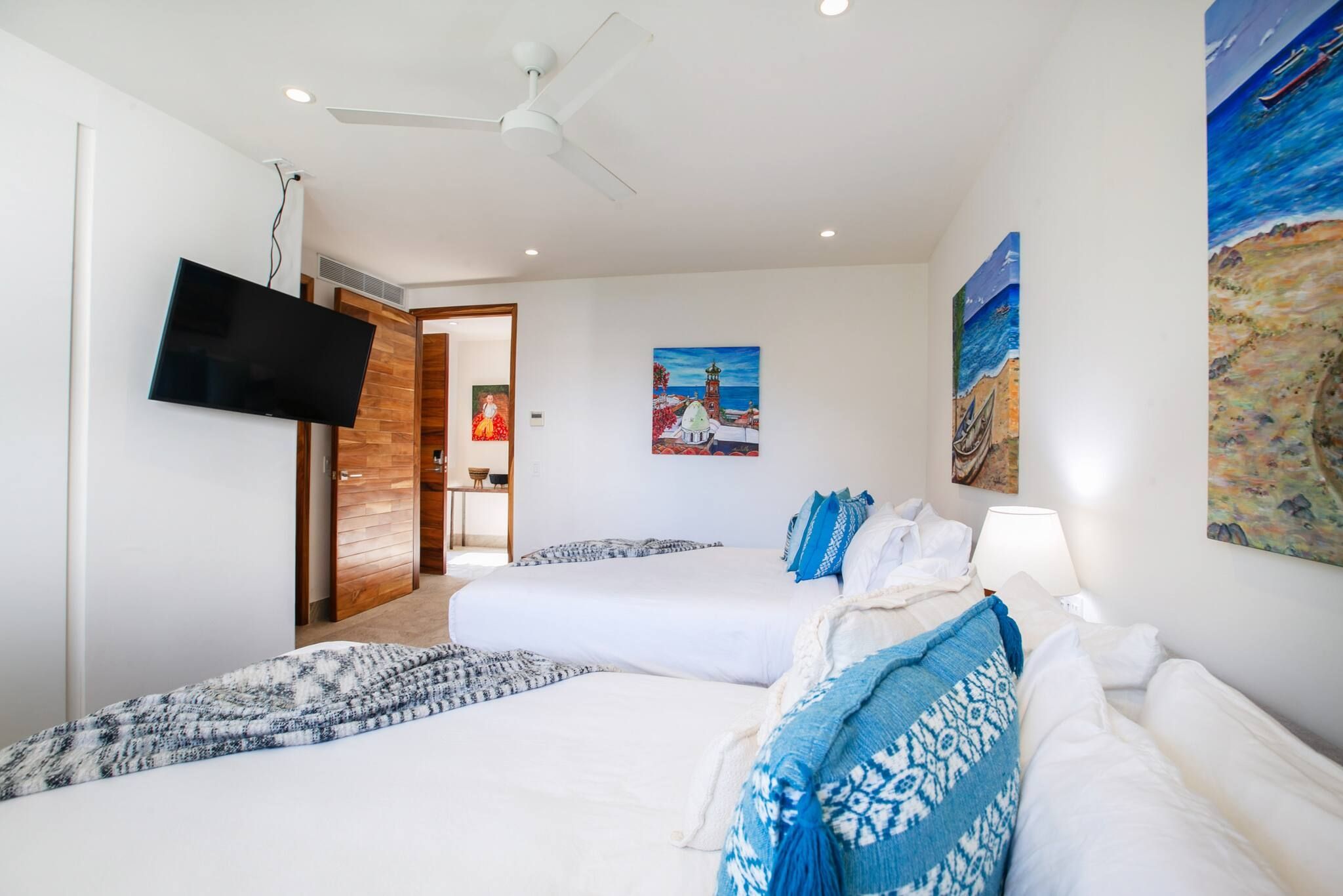 Ein Hotelzimmer mit zwei Betten, einem an der Wand montierten Fernseher und Kunstwerken, die Küstenlandschaften zeigen.