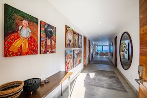 A hallway with a series of paintings on the wall, a wooden bench, and a woven basket.