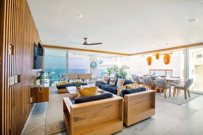 Un salon moderne avec une grande fenêtre, des meubles en bois et une vue sur l’océan.