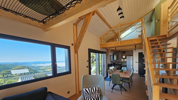 Amplia zona de estar con un ventanal que ofrece vistas al campo, un rincón de descanso acogedor y una escalera de madera que conduce a un nivel superior.