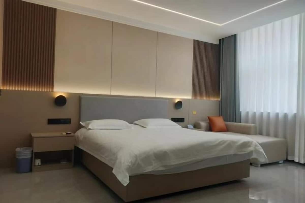 Un dormitorio moderno con una cama grande, mesitas de noche, un sofá y un amplio ventanal con cortinas.
