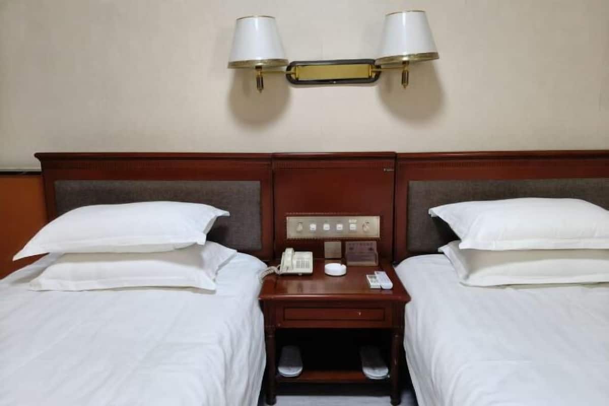 Una habitación de hotel con dos camas, una mesita de noche con teléfono y lámpara, y una luminaria fijada a la pared.