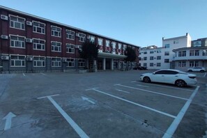 A parking lot with marked parking spaces and a building with multiple windows and air conditioning units. - Dongguan Hotel (Tumen)