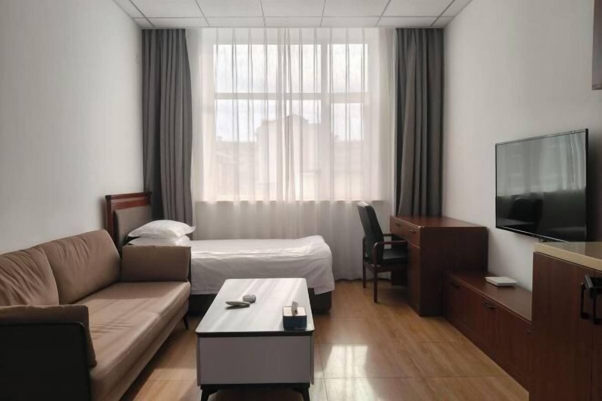 Una habitación de hotel con cama, sofá, escritorio, televisión y ventana con cortinas.