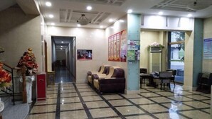 A lobby with a checkered floor, a reception desk, a sofa, and a staircase with a decorative railing. - Dongguan Hotel (Tumen)