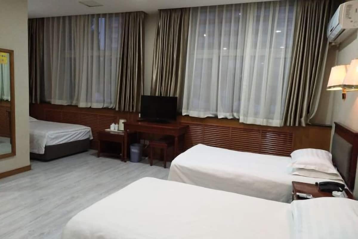 Habitación de hotel con dos camas, televisión, escritorio y ventana con cortinas.