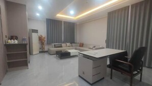 A modern living room with a sofa, a coffee table, a desk with a chair, and a wardrobe. - Dongguan Hotel (Tumen)