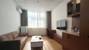 A modern hotel room with a sofa, a small table, a TV, and a wooden cabinet. - Dongguan Hotel (Tumen)