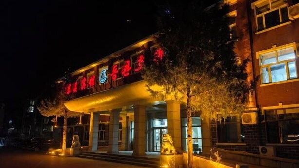 A hotel entrance with a red sign, a covered walkway, and a statue. - Dongguan Hotel (Tumen)
