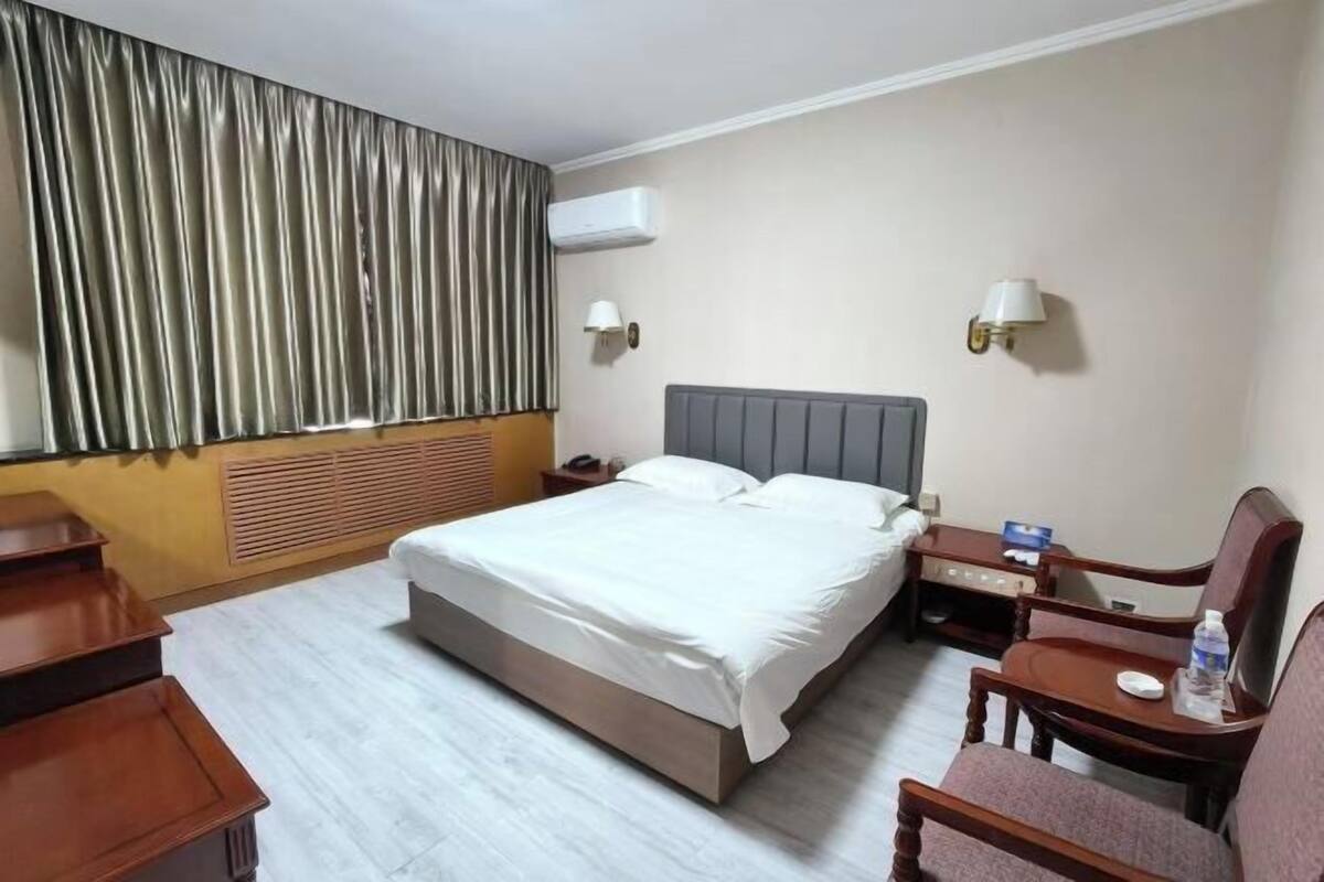 Habitación de hotel con cama, mesitas de noche, una silla, escritorio y equipo de aire acondicionado.