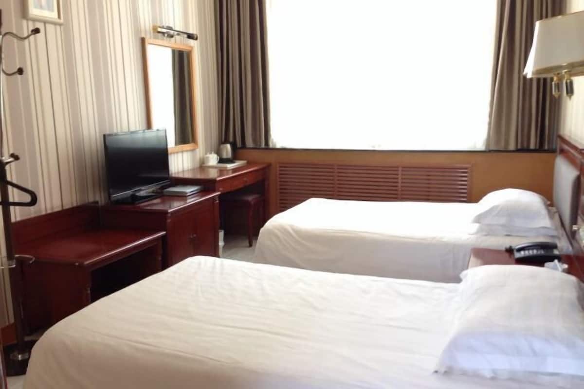 Una habitación de hotel con dos camas, un escritorio, un televisor y una ventana con cortinas.