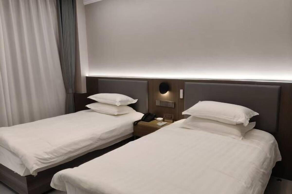 Habitación de hotel con dos camas individuales, una mesita de noche con teléfono y una lámpara de pared.