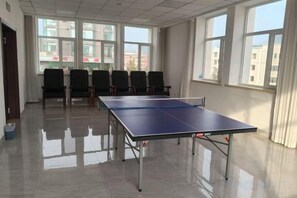 A room with a ping pong table, chairs, and large windows. - Dongguan Hotel (Tumen)