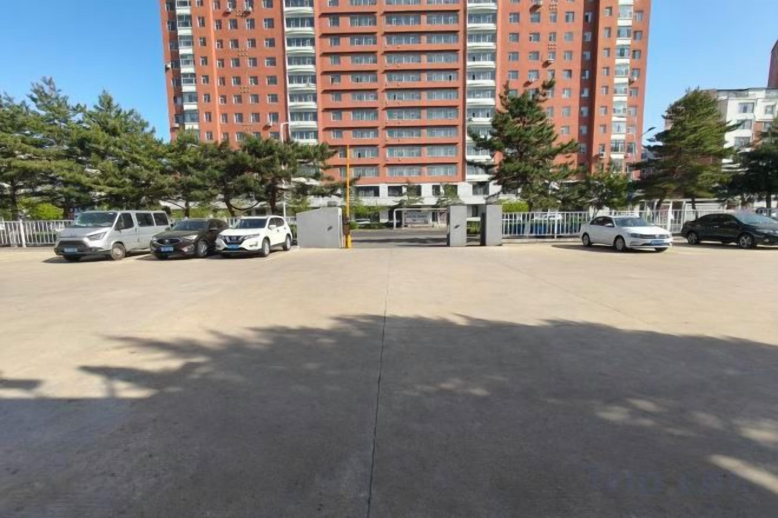 A parking lot with several cars, a tall red building in the background, and trees.