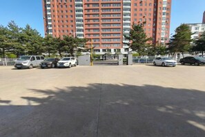 A parking lot with several cars, a tall red building in the background, and trees. - Dongguan Hotel (Tumen)