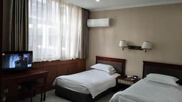 A hotel room with two beds, a desk with a television, an air conditioner, and two wall-mounted lamps.