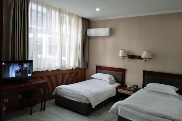 Habitación de hotel con dos camas, un escritorio con televisor, aire acondicionado y dos lámparas de pared.