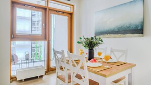 A dining area with a wooden table, white chairs, a potted plant, and a painting on the wall. - P&O Apartments Arkadia 1 (Warsaw)