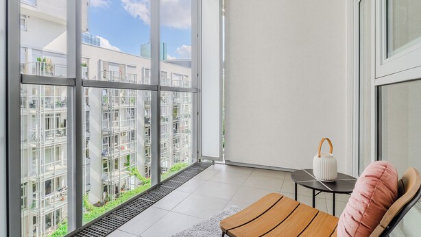 A balcony with a view of a modern building complex, a white lamp, and a cushioned chair. - P&O Apartments Arkadia 1 (Warsaw)