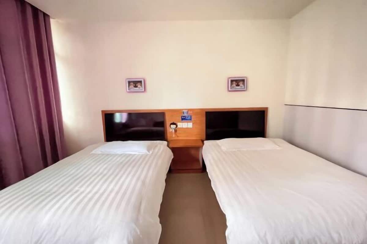 Quarto de hotel com duas camas de solteiro, cabeceira de madeira, mesa de cabeceira e uma pequena mesa.